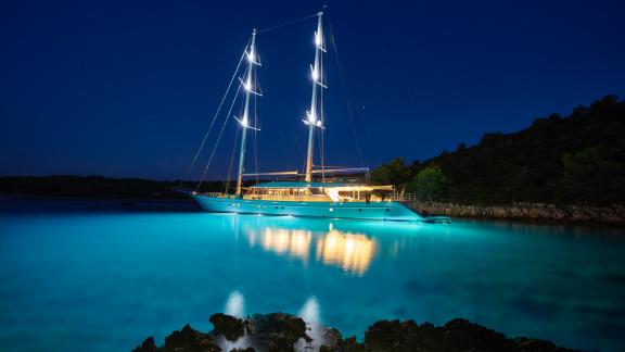 With its bright spotlights, the luxury yacht illuminates the crystal clear water under a magnificent starry sky.